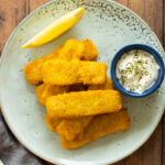 A stack of fish fingers with sauce and a lemon wedge.