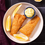 Breaded fish fillets with lemon wedges and sauce.